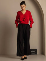 Model in red V-neck silk-wool blouse and black straight-leg pants with side pockets