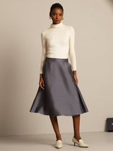 Model wears cream silk-wool blend turtleneck and gray A-line midi skirt with side pockets