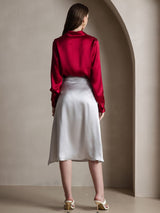 Back view of a woman wearing a red silk long sleeve lapel collar blouse with a silver satin skirt