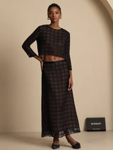 Model wearing a black silk grid A-line high-waist long skirt with matching sheer top