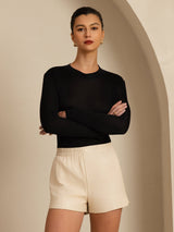 Woman wearing black silk mock neck long sleeve top with slim fit and cream shorts