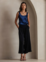 Blue sleeveless U-neck silk tank top with satin finish, styled with black wide-leg pants