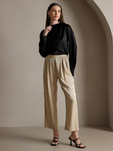 Black silk boat neck blouse with long sleeves and pearl button details, styled with beige pants