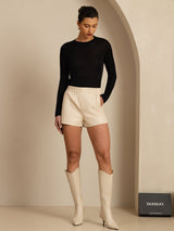 Woman wearing a black long sleeve mock neck top with cream shorts and boots